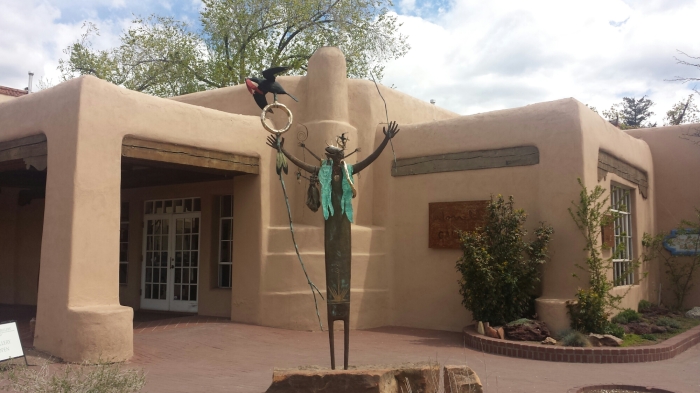 a pueblo house with a bronze warrior statue in front of it