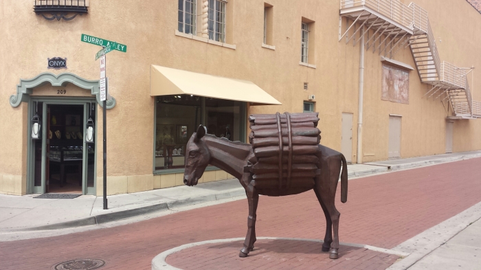 a statue of a donkey with logs on it's back, in the middle of a cobble stone street